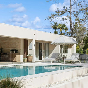 Modern house with a pool and outdoor furniture under a clear blue sky, with a sage green pool sign.