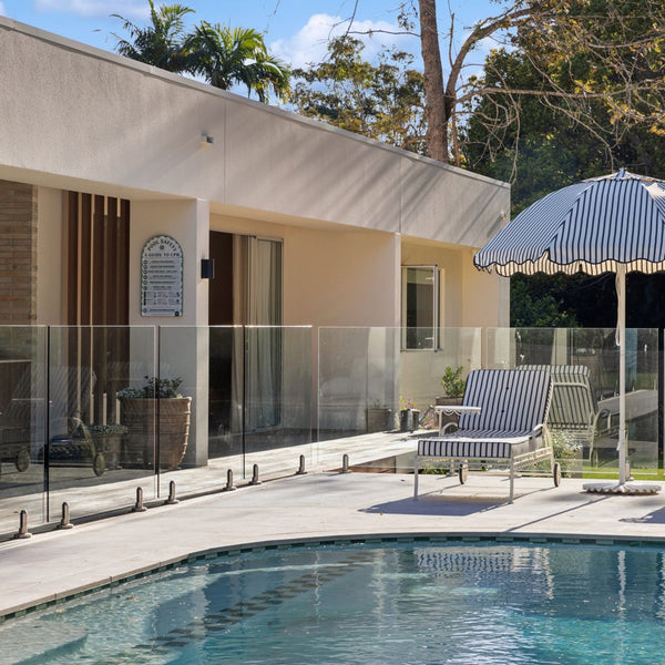 Pool area with lounge chairs and an umbrella next to a house, with a sage green pool sign.